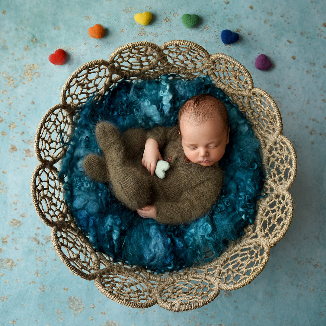 Newborn photography backdrops - a top-down shot of a newborn baby inside a circular basket with rainbow felt hearts above it.