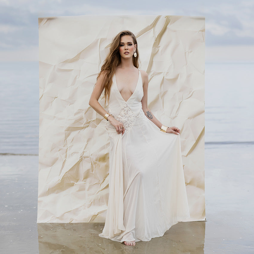 Woman in a white dress standing on a beach with a textured backdrop. 